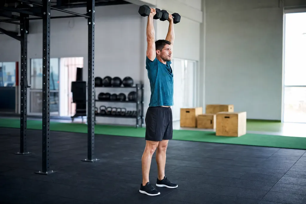 Man at the top of a dumbbell push press in a functional gym