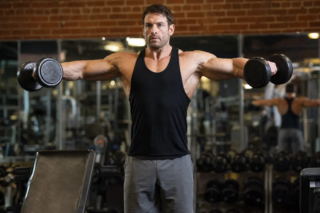 Muscular man doing a dumbbell lateral raise in an old school gym